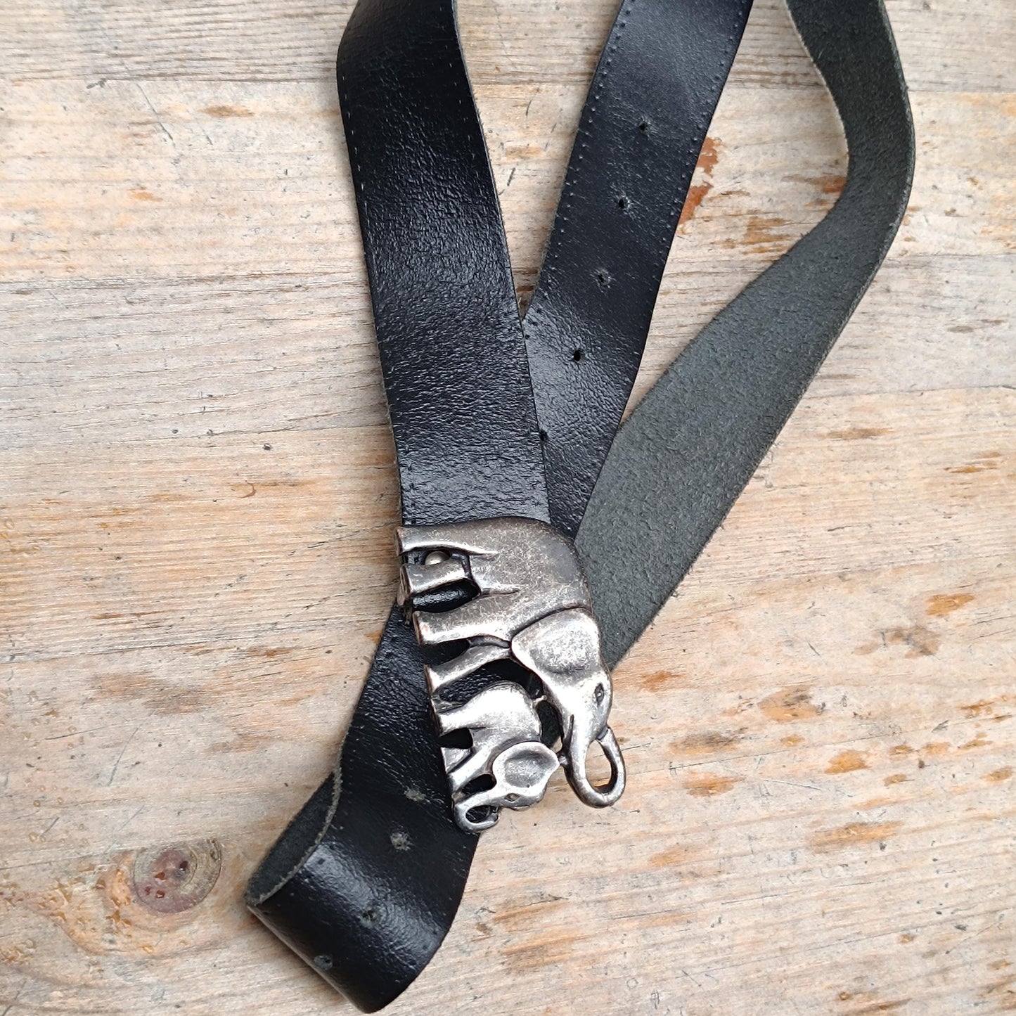 Full-length image of a 70s vintage handmade black leather belt with adjustable holes and a detailed elephant buckle closure