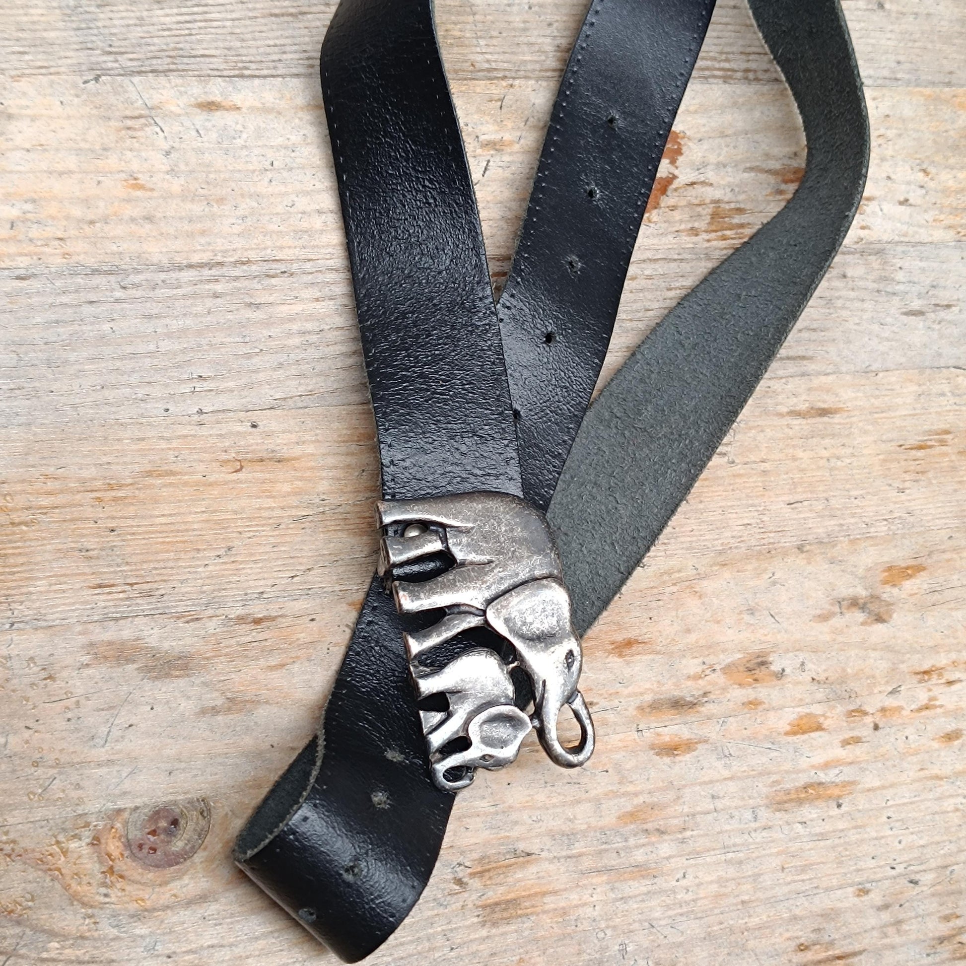 Full-length image of a 70s vintage handmade black leather belt with adjustable holes and a detailed elephant buckle closure