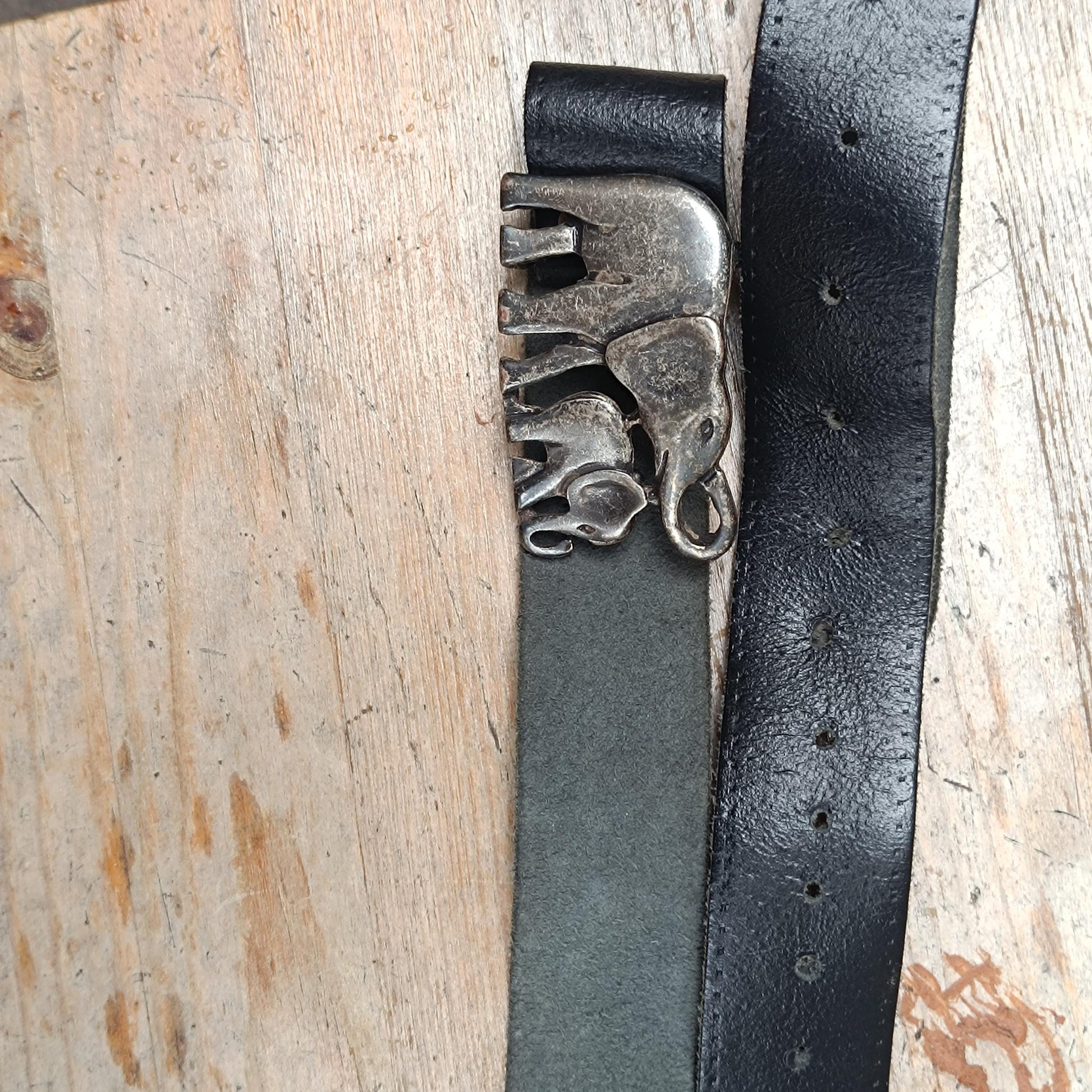 Artistic flat lay of an Indian-inspired vintage leather elephant buckle belt on a wooden surface, capturing the bohemian and earthy aesthetic