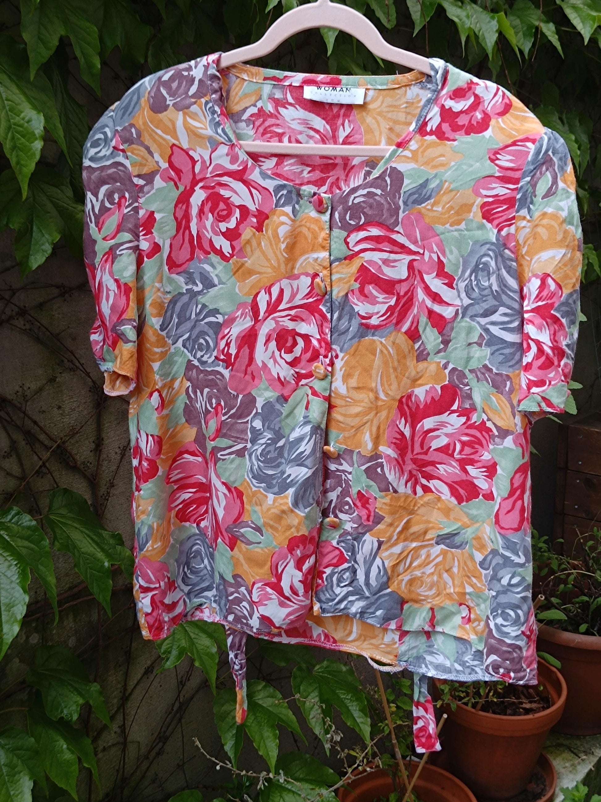 Vintage 90s colorful floral blouse with puff sleeves is photographed on a hanger Infront of green background.