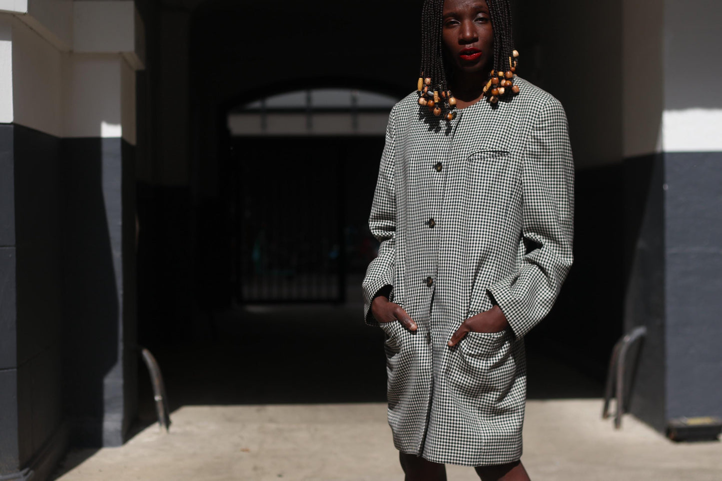 Front view of a vintage black and white checkered blazer dress with structured shoulders and oversized buttons, styled as a statement outerwear piece on a female model in an urban outdoor environment