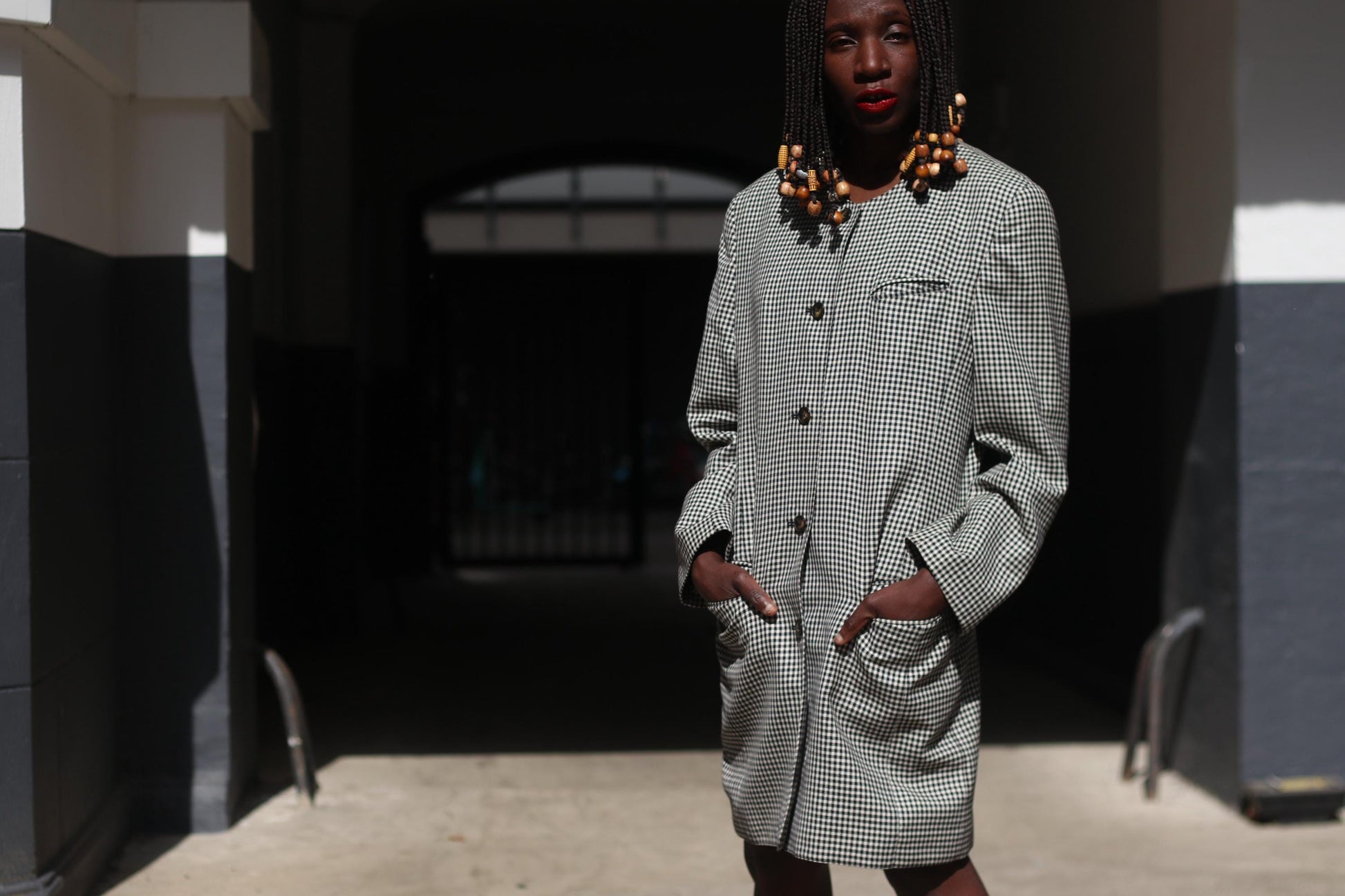 Front view of a vintage black and white checkered blazer dress with structured shoulders and oversized buttons, styled as a statement outerwear piece on a female model in an urban outdoor environment