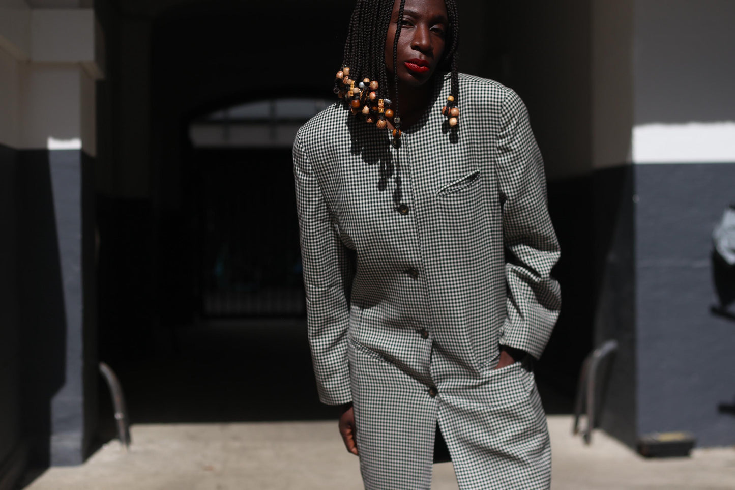 Female model with beaded braids wearing a 90s checkered vintage blazer as a dress, buttoned up and paired with boots and shows off  a confident stance