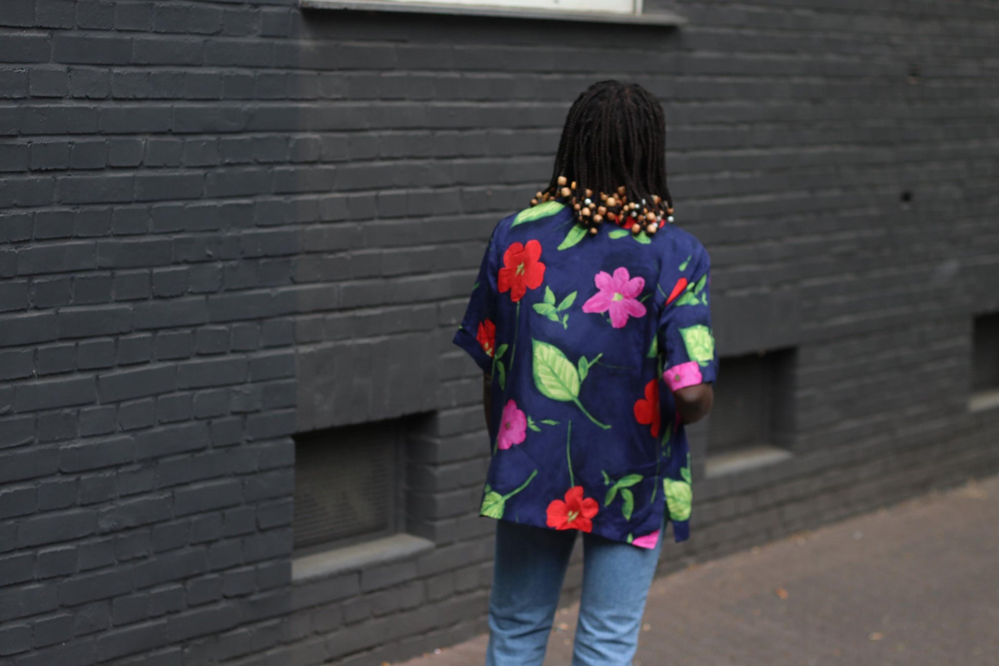 Back view of vintage navy floral blouse with bold hibiscus print om a model Infront of a grey brick wall