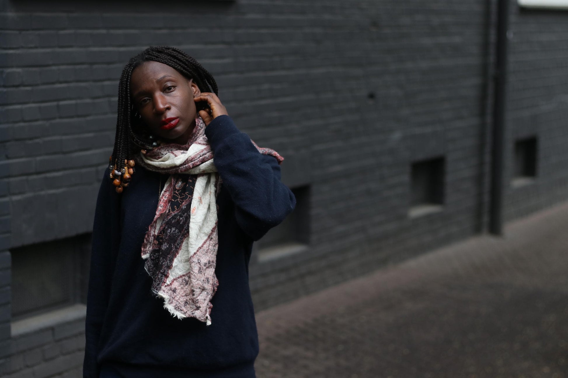 A female model in a boho chic multicolored scarf standing in front of a grey brick wall