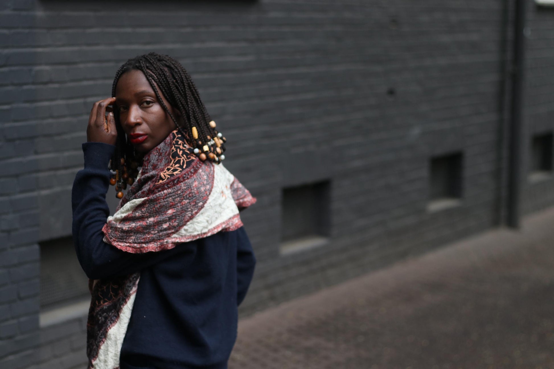 side view of a retro patterned scarf worn  by a female model, in front of a grey textured brick wall. The image highlights   the unique print and color palette of the boho oversized scarf.