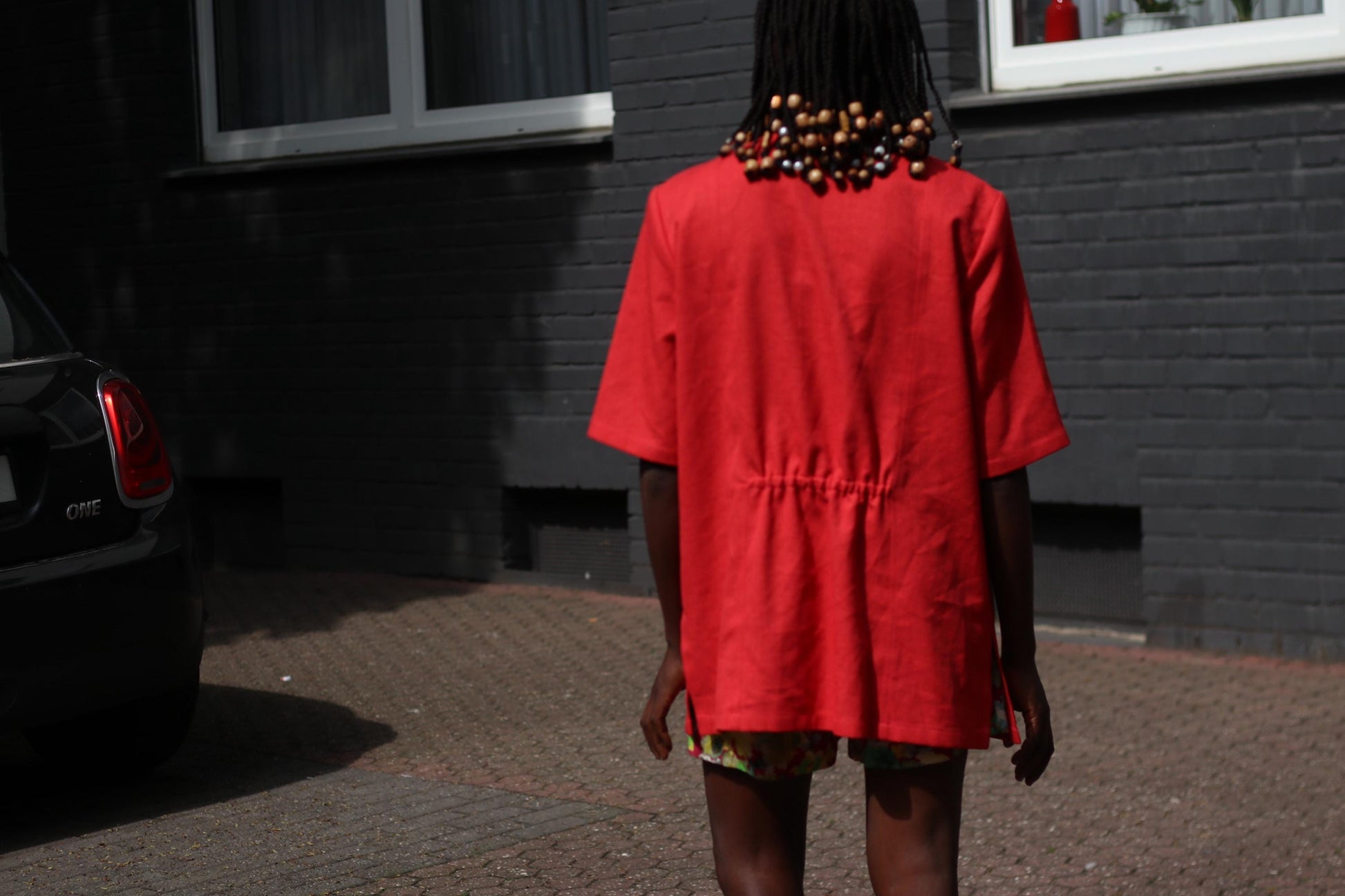 Back view of a female model wearing a vintage 90s Short-Sleeve Blazer by Mark Wald as a short dress photographed in front of a grey brick wall.  The image showcases the  rouched detail at the back of the blazer