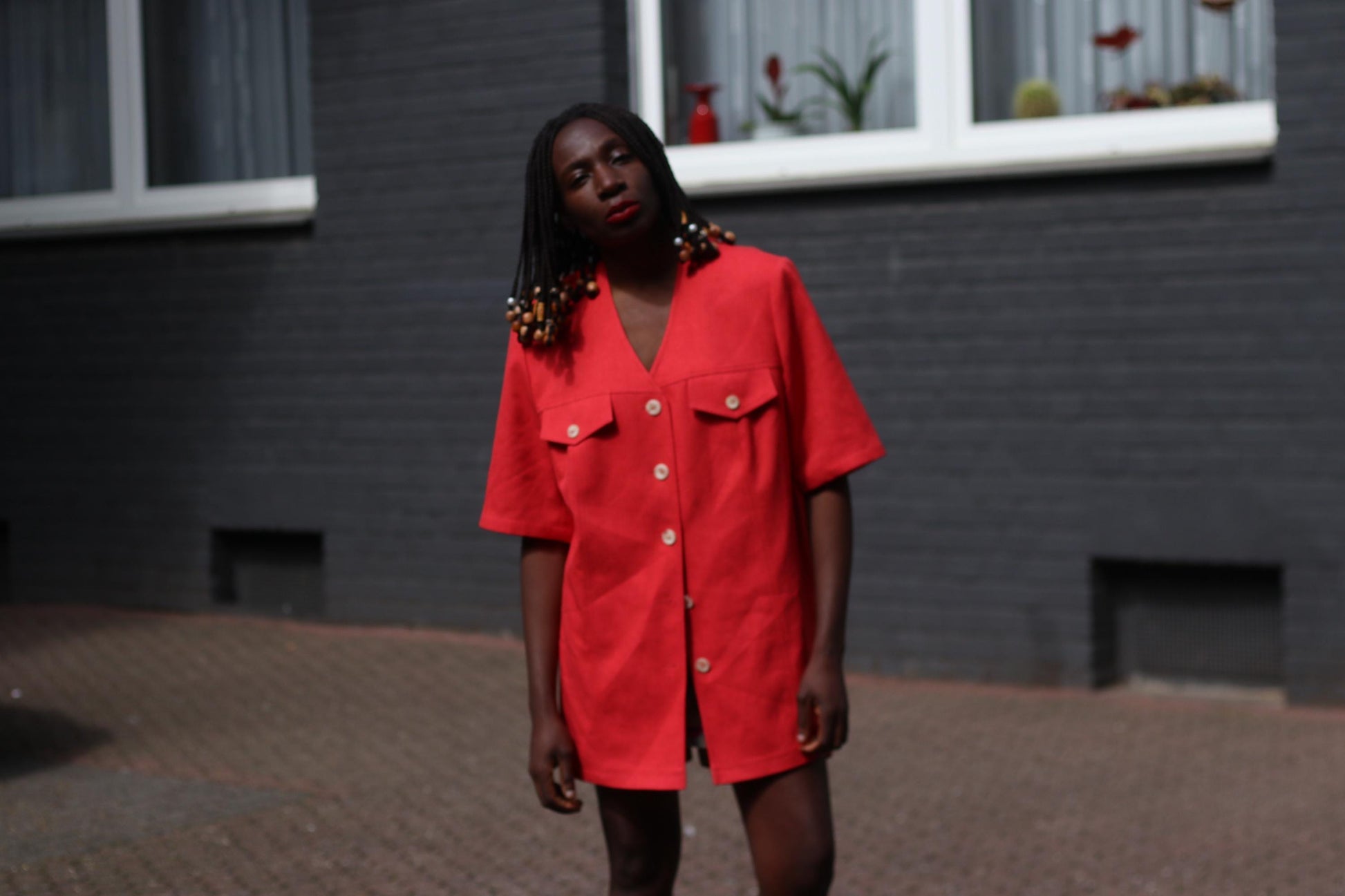 Female model wearing a vintage 90s Short-Sleeve Blazer by Mark Wald as a mini retro dress, photographed in front of a grey brick wall.  The image showcases the  bold V-Neck silhouette, buttons and breast pockets