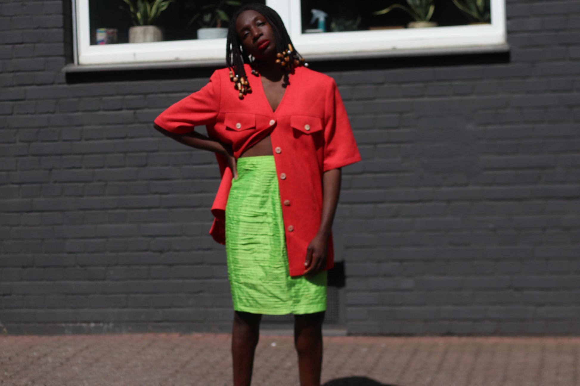 Female model wearing a vintage 90s Short-Sleeve Blazer by Mark Wald with a neon green knee-length skirt photographed in front of a grey brick wall with a  white window sill visible.  The image showcases the  bold V-Neck Jacket as a lightweight choice for suiting up in the summer
