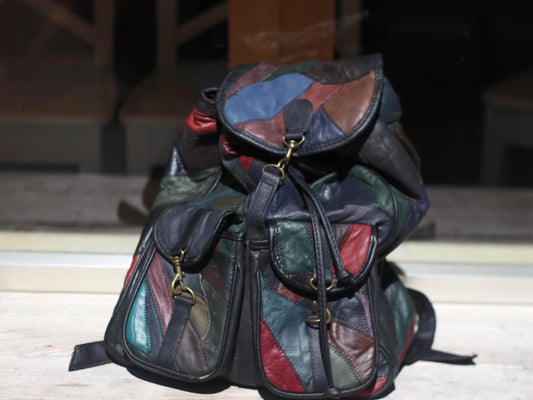 Vintage 1980s multicolor leather patchwork backpack photographed on a wooden surface upright leaning on a glass background