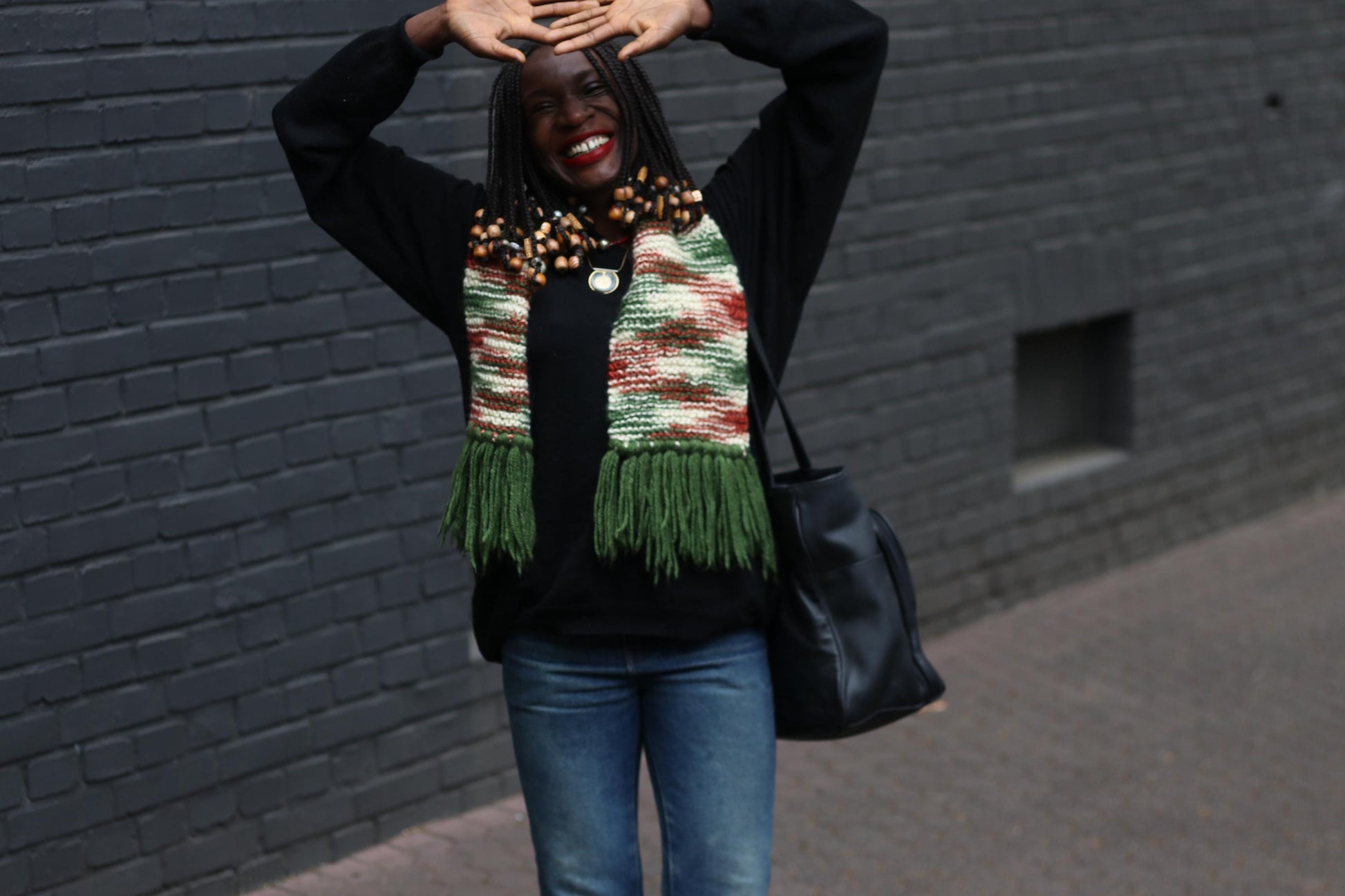 70s handknitted scarf with multicolor yarn and fringe detailing, styled with casual winterwear and big  bag on a female model captured outdoors against a grey brick wall
