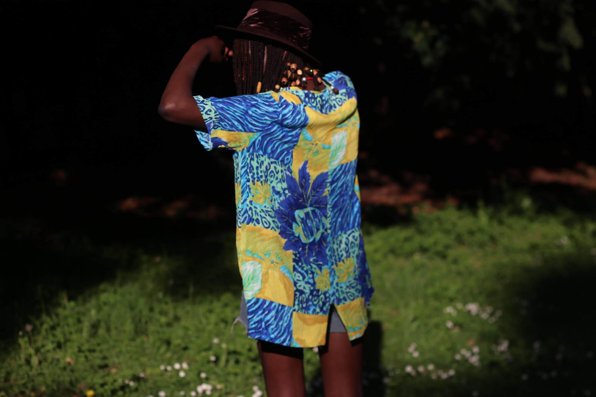 A back view of a female model with beaded braids in a bold vintage 90s tropical button-up shirt with vibrant floral and animal prints, modeled in natural light.
