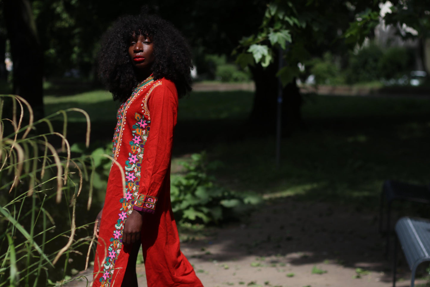 Female Model with curly black hair in a romantic 70s embroidered vintage maxi dress posing outdoor near a lake in a park