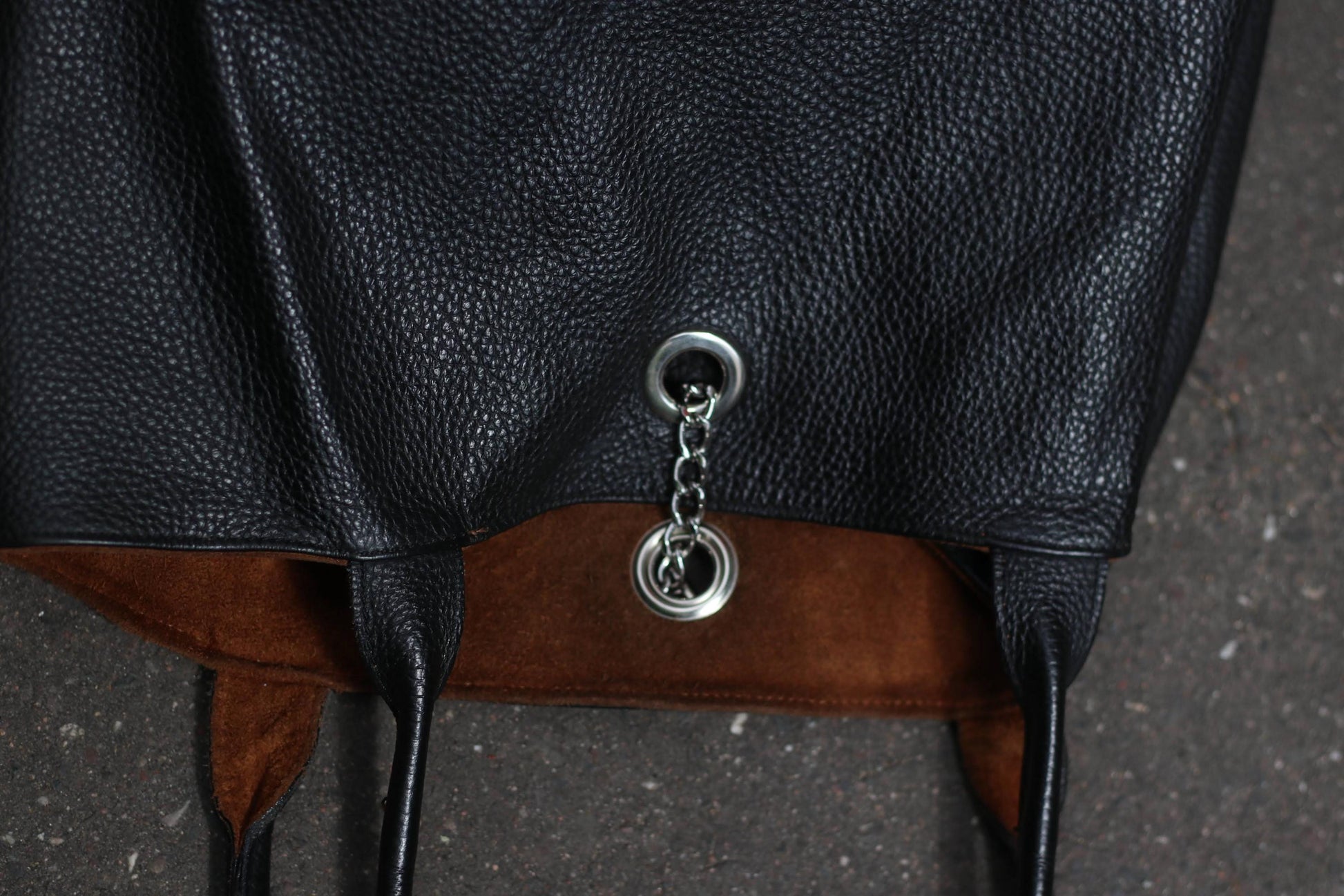 close up of silver chain detail on a  vintage black, pebbled leather tote bag with a brown lining laying on a dark textured surface.