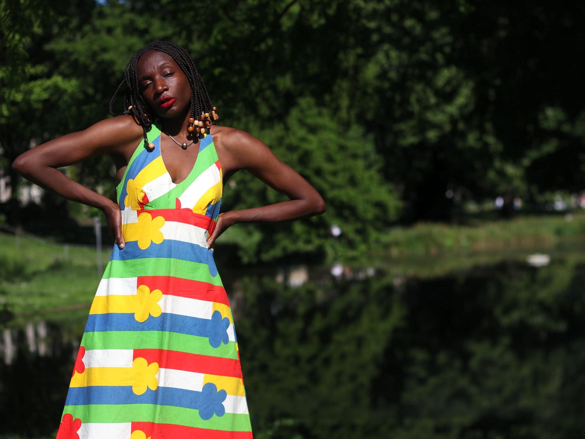 Woman with beaded braids wearing a bold 1970s floral halterneck dress made in Finland with primary-colored stripes in a sunny park