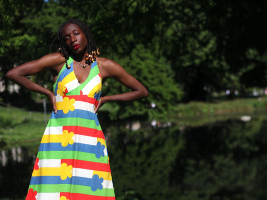 Woman with beaded braids wearing a bold 1970s floral halterneck dress made in Finland with primary-colored stripes in a sunny park