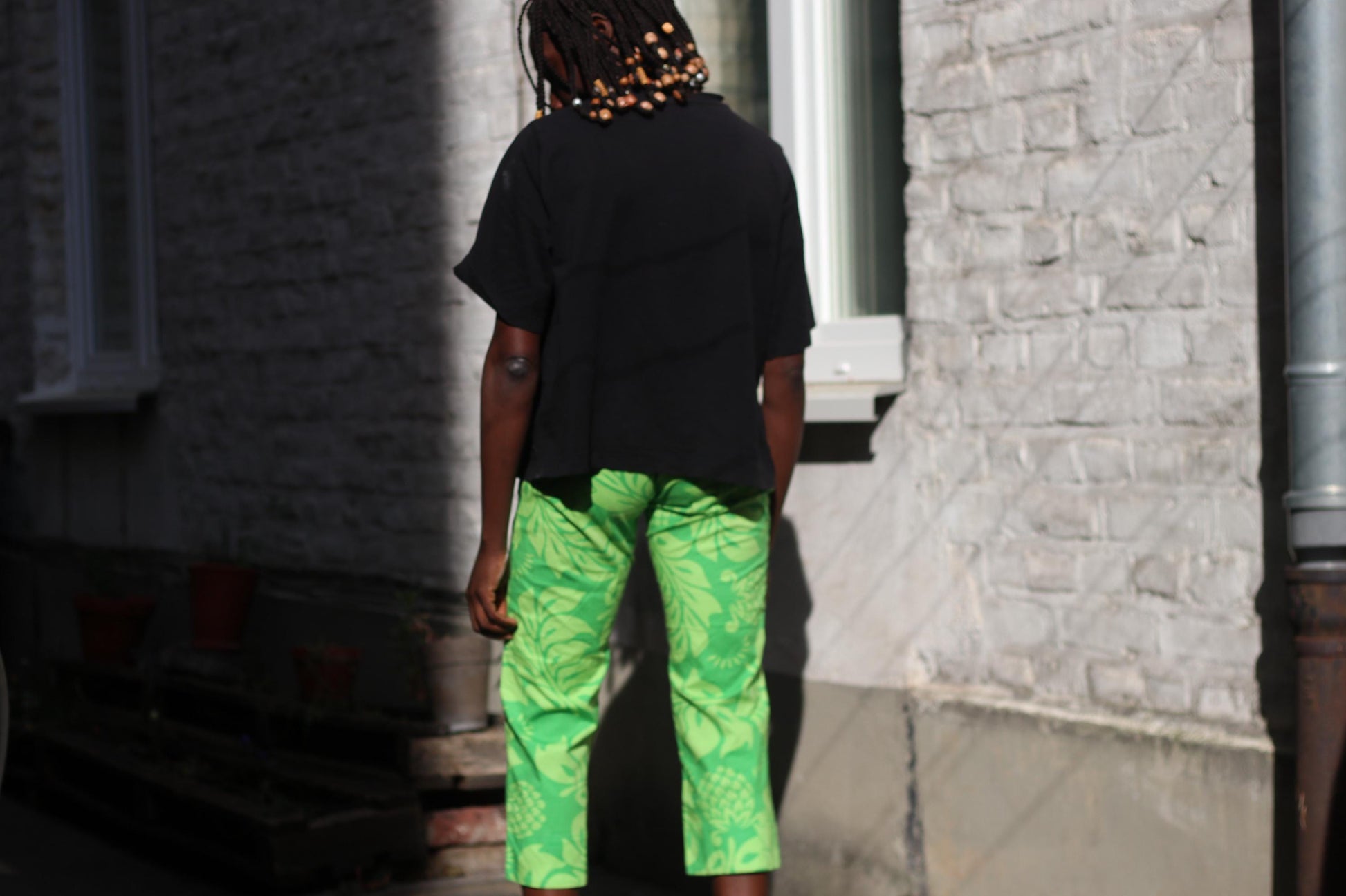 Female Model in green patterned cropped pants by quicksilver is, photographed outside against architectural elements.