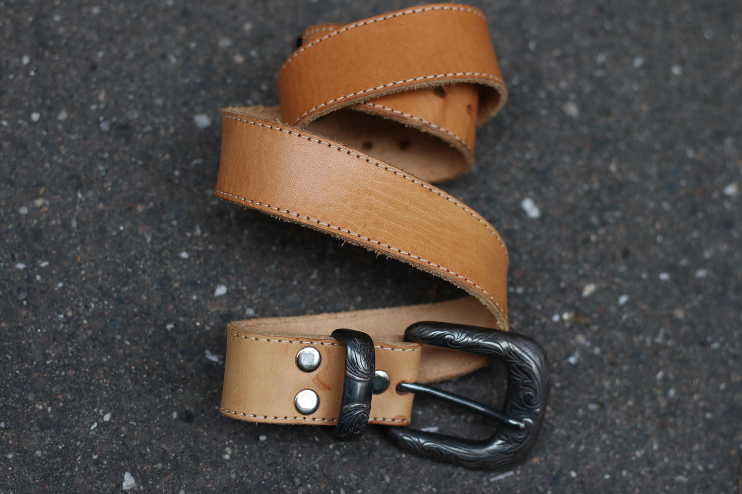 A vintage light brown leather belt with a boho chic cowgirl vibe is photographed, partially coiled, showing the buckle and strap details.