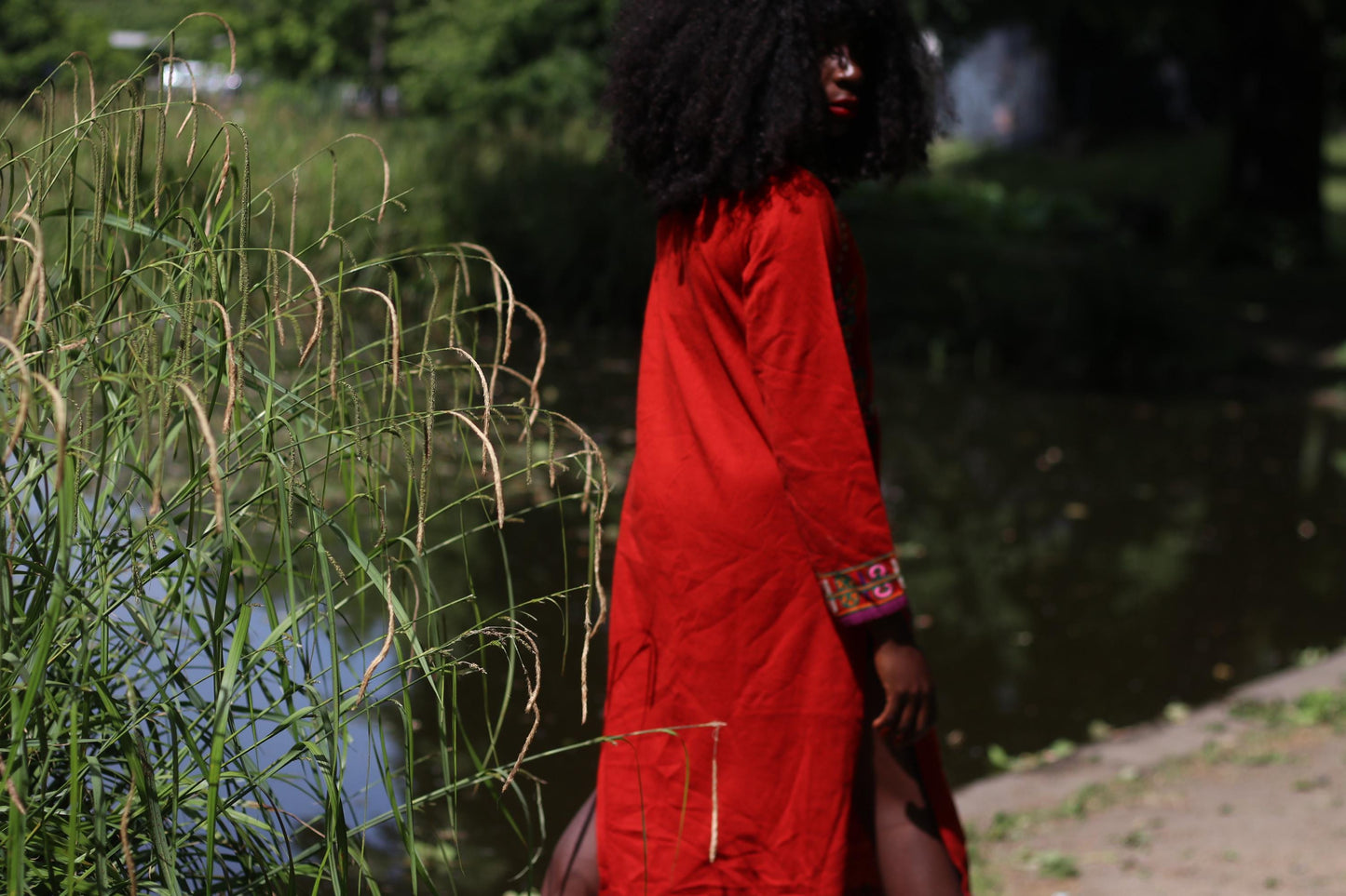 A back view of a female Model in a romantic red embroidered vintage dress posing outdoors near a body of water