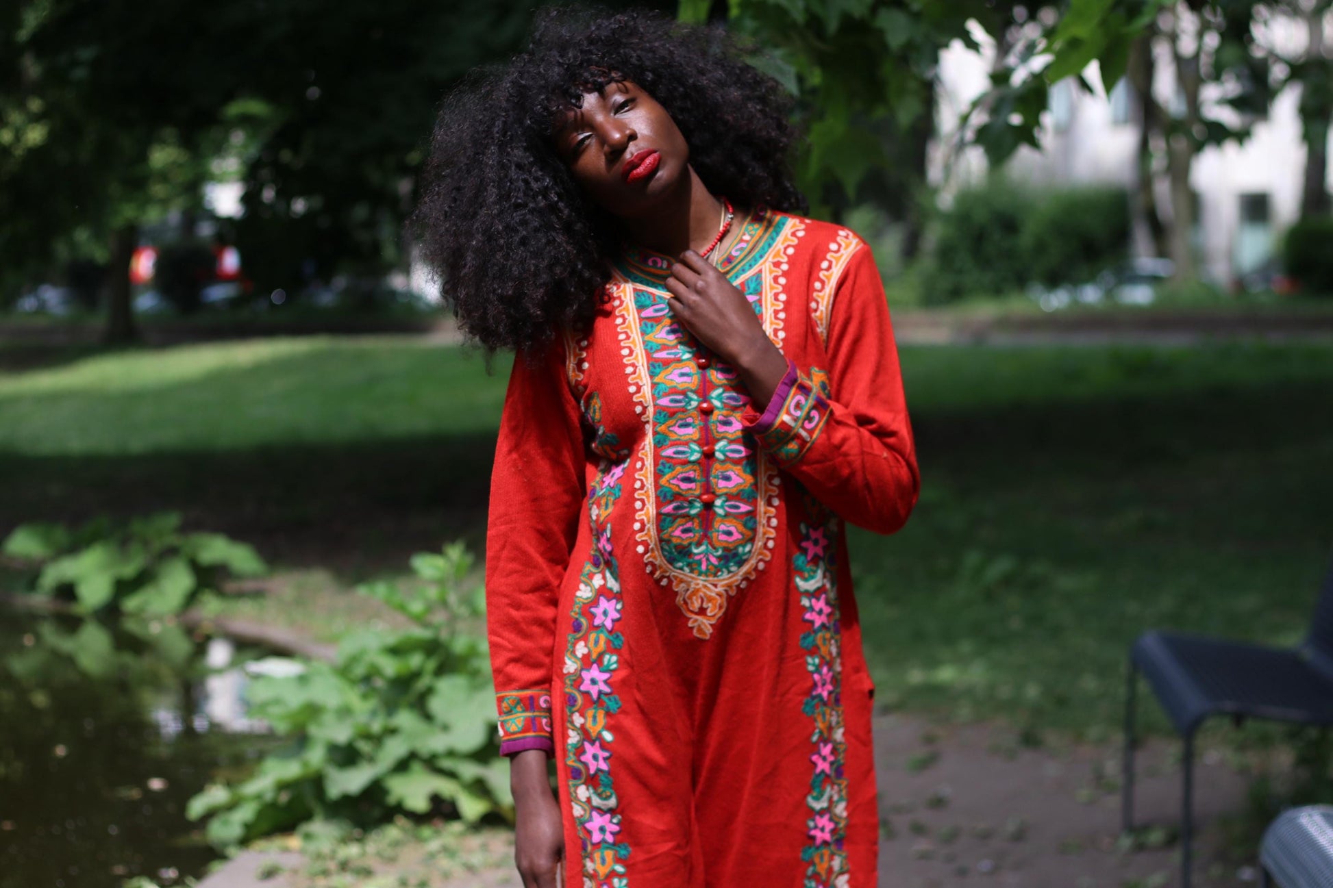 Artisanal red vintage festival maxi dress styled  on a female model with natural curls and bold lipstick photographed outdoors in a park with plenty of greenery