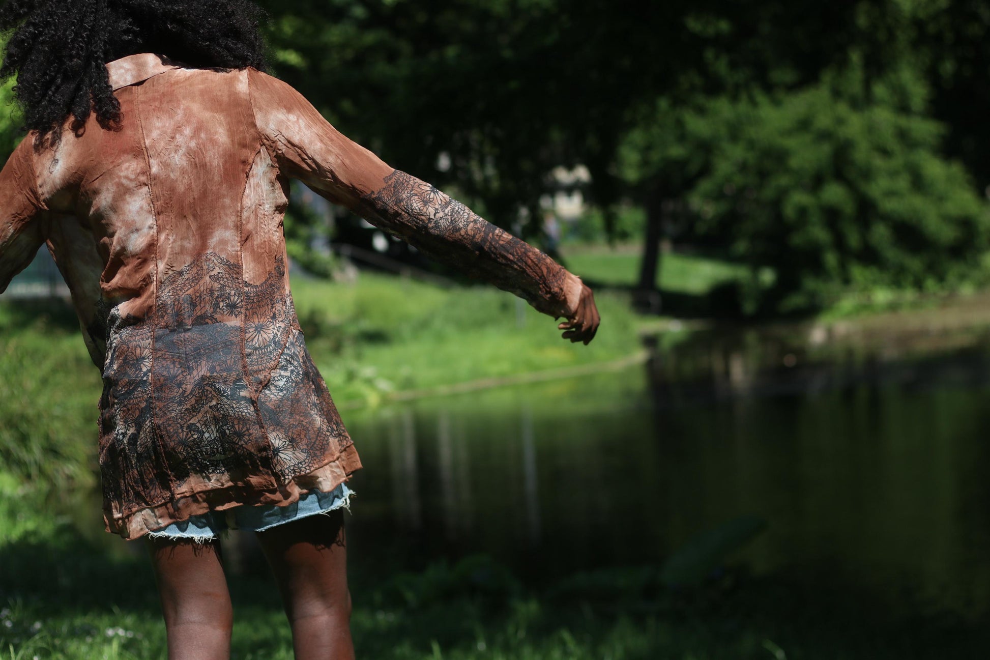 Joyful female Model with curly black hair wearing a vintage sheer brown BibA blouse with floral print photographed outdoors with lake backdrop