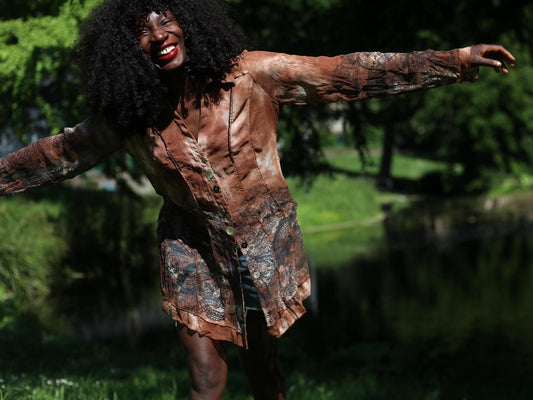 Female Model  with curly black hair wearing sheer brown BibA blouse outdoors with lake backdrop