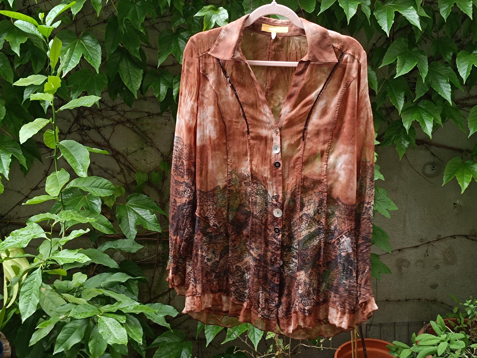 Vintage retro blouse in brown with floral print photographed hanging against a leafy background outdoors