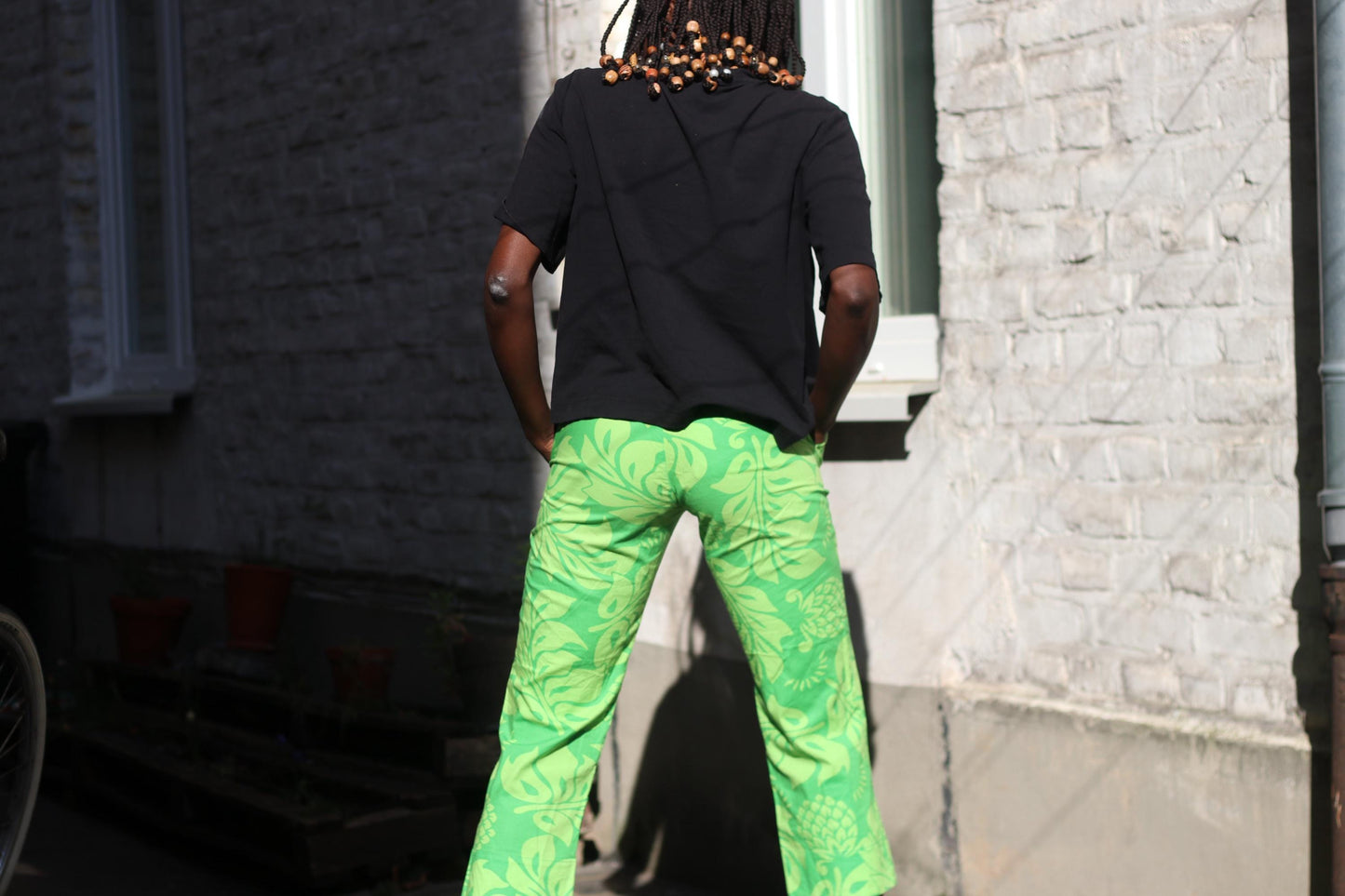 back view of a female model in a pair of summer green patterned cropped pants by Quiksilver, photographed outside against architectural elements.