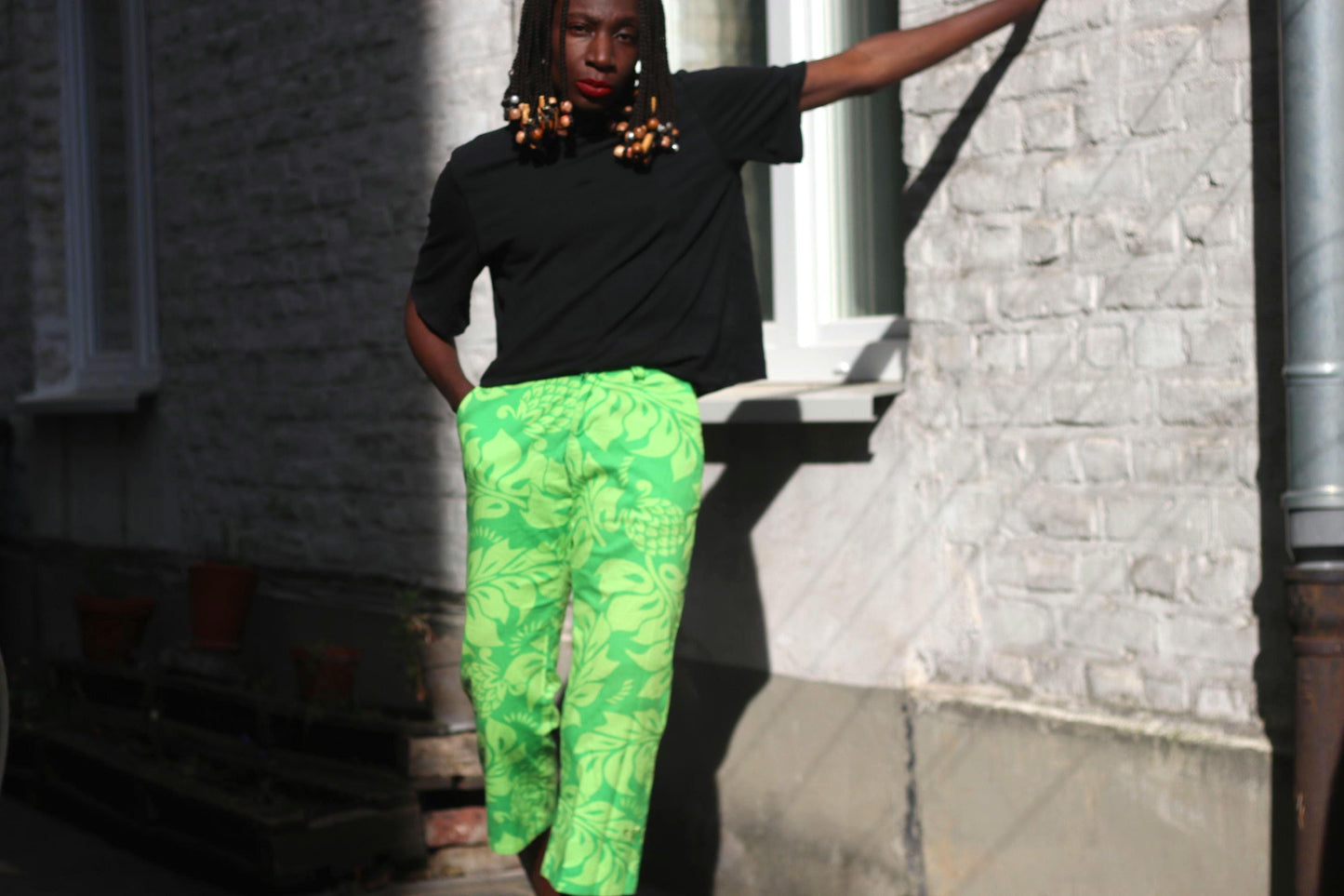 female model in a vintage Y2K quicksilver patterned green pants captured outdoors against a light-colored wall. Model has one hands in her cropped pants