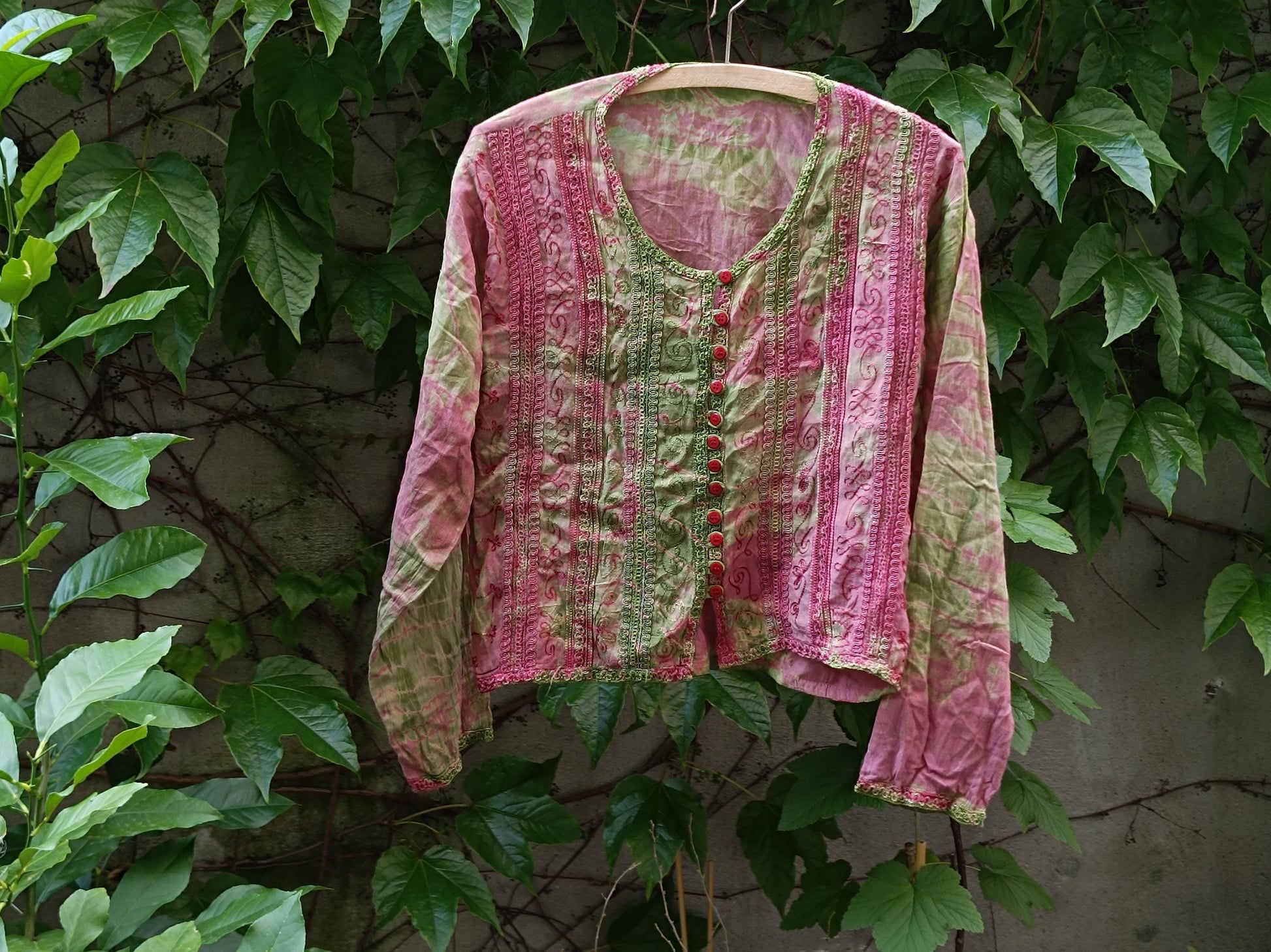 Retro tie-dye boho blouse with pink and green patterned photographed hanging outdoors on a clothing line with leaves in the background. The still life image showcases the print and texture of the retro long-sleeved top.