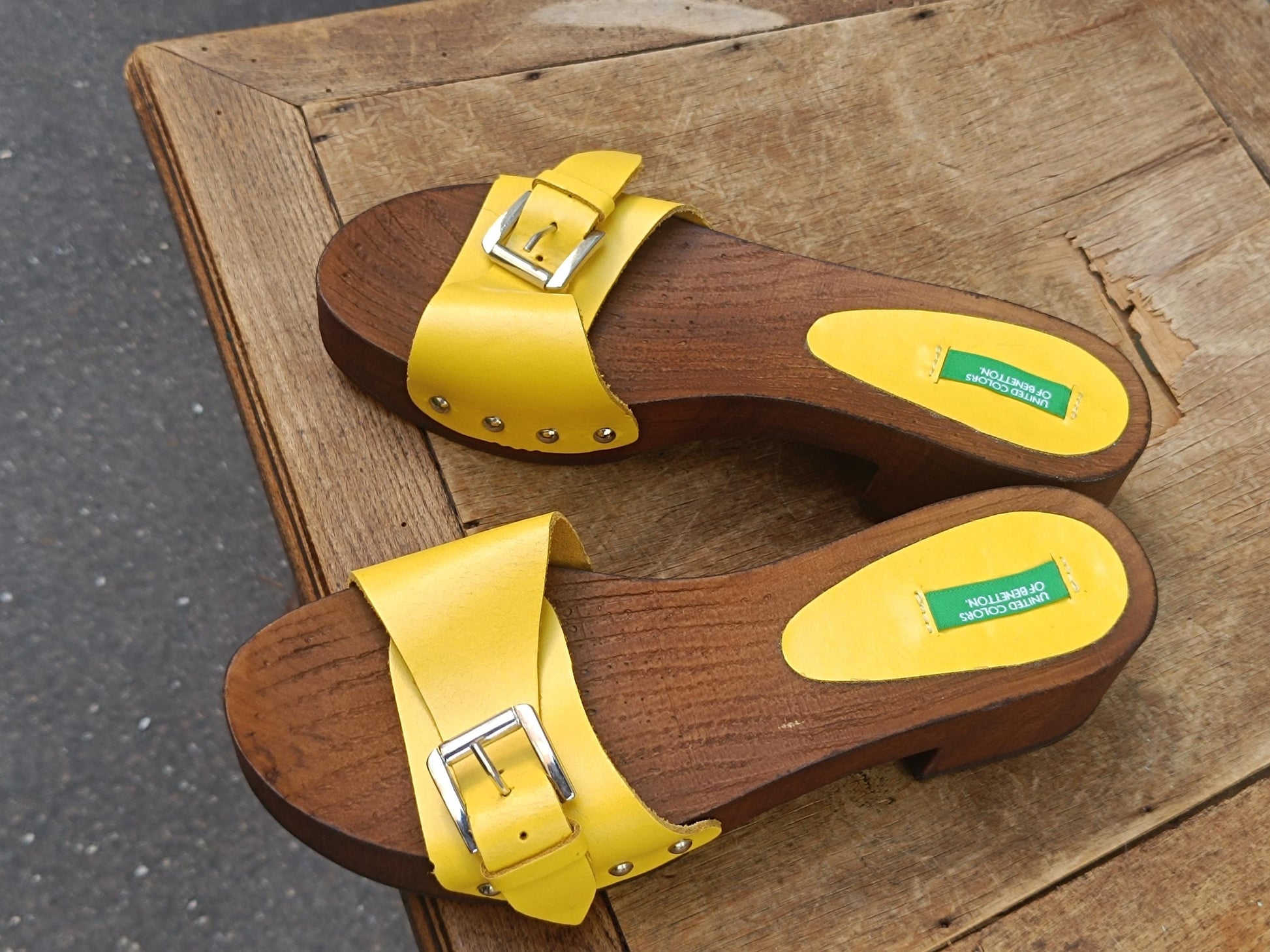 Pair of bright yellow y2k Benetton wooden clogs on a rustic wooden table.