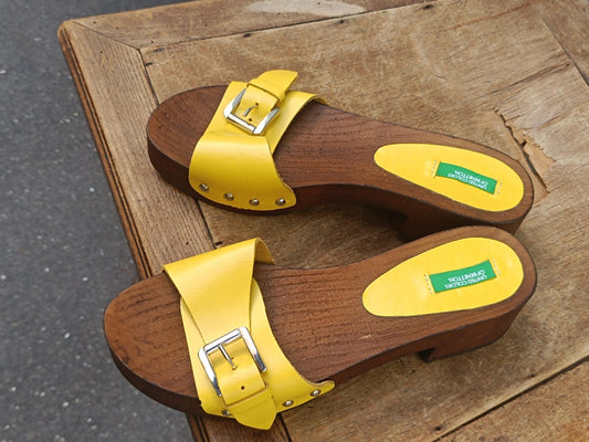 Pair of bright yellow y2k Benetton wooden clogs on a rustic wooden table.
