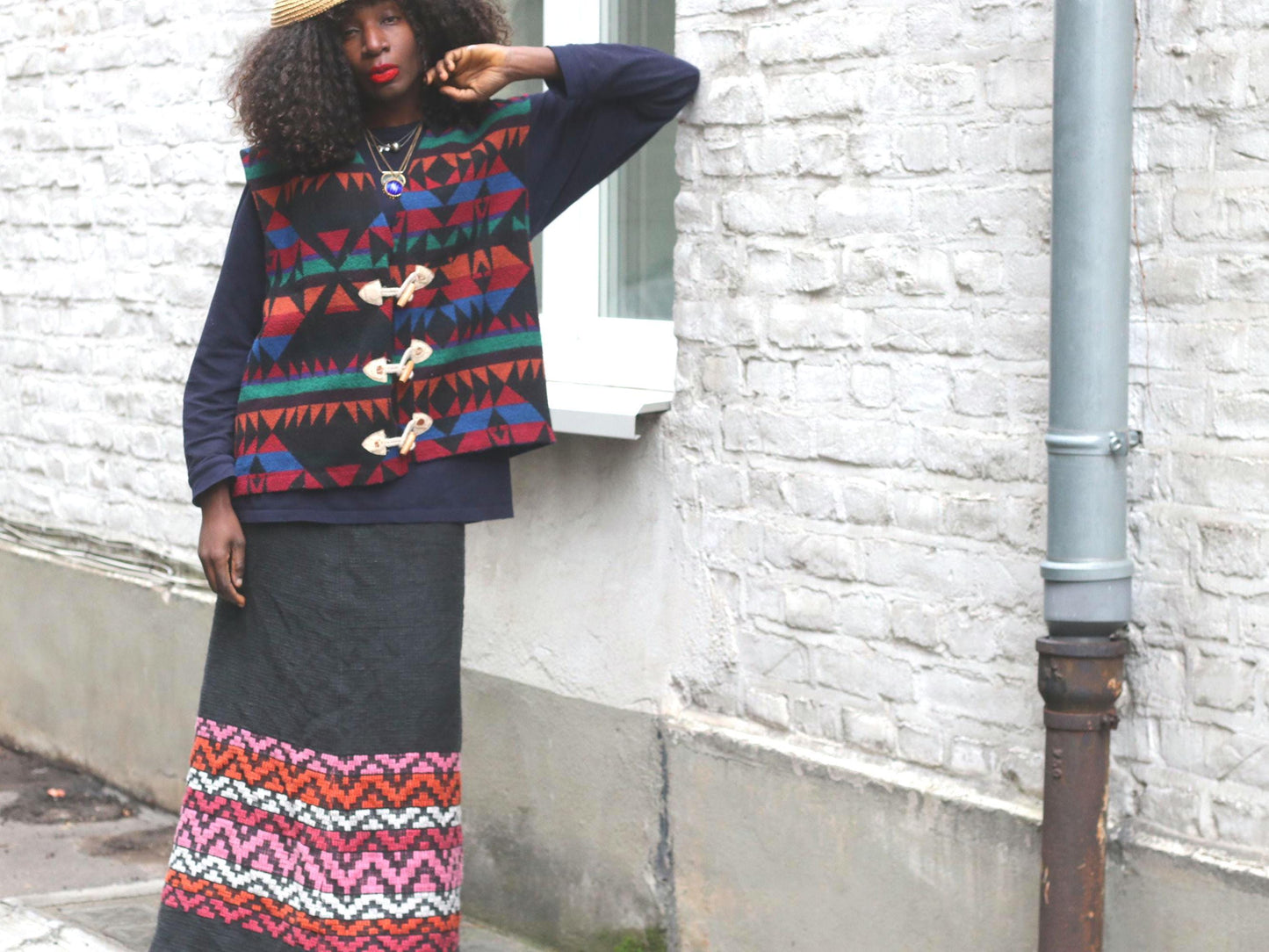 Femal model wearing a  vintage black knit maxi skirt with a wide, colorful geometric pattern band at the bottom hem photographed outdoors against a white brick exposed wall
